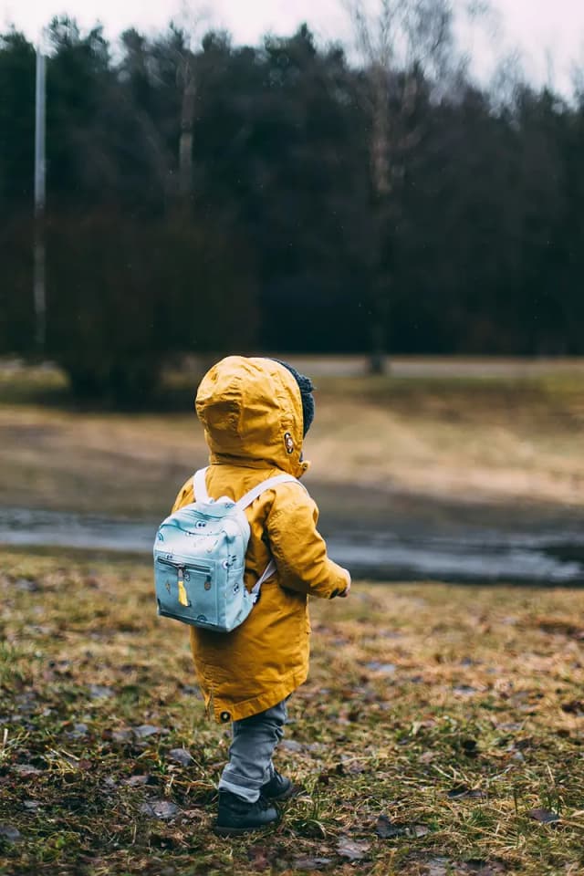 image d'un enfant avec vu de dos qui marche vêtu d'une doudoune jaune avec une capuche et un sac à dos